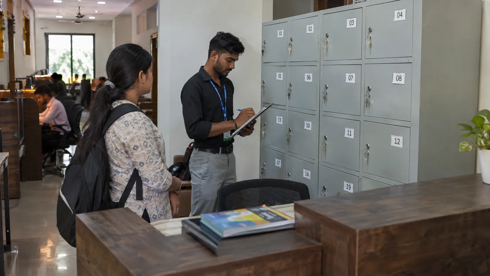 Indian study-library staff member reviewing numbered lockers with an adult member