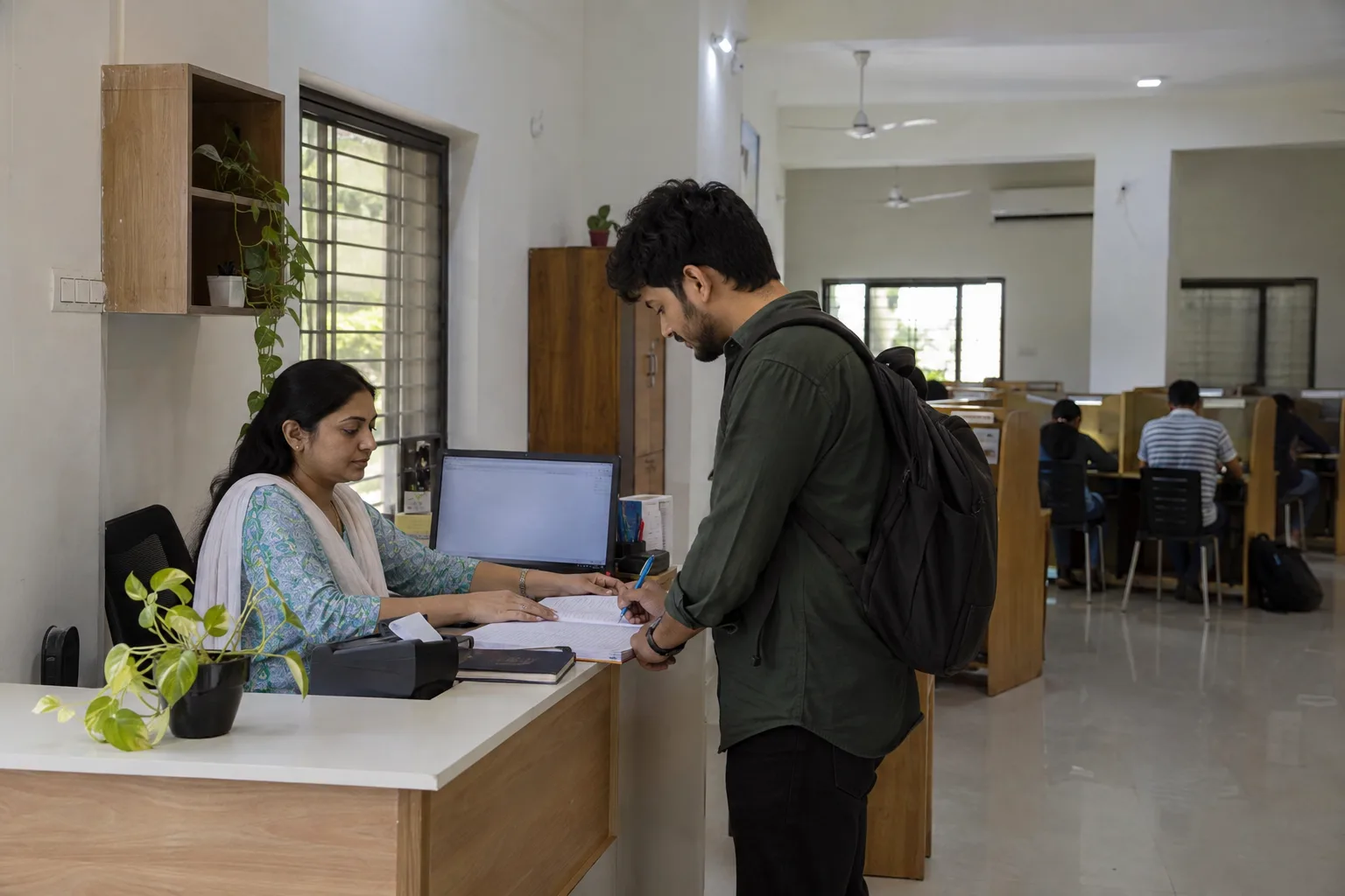 Indian study-library receptionist assisting an adult member with a membership renewal