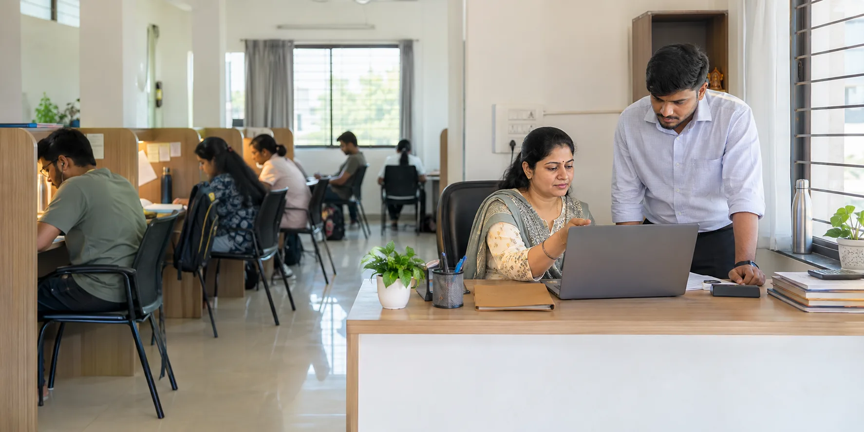 Indian study-library owner and staff reviewing software operations with adult members studying in the background